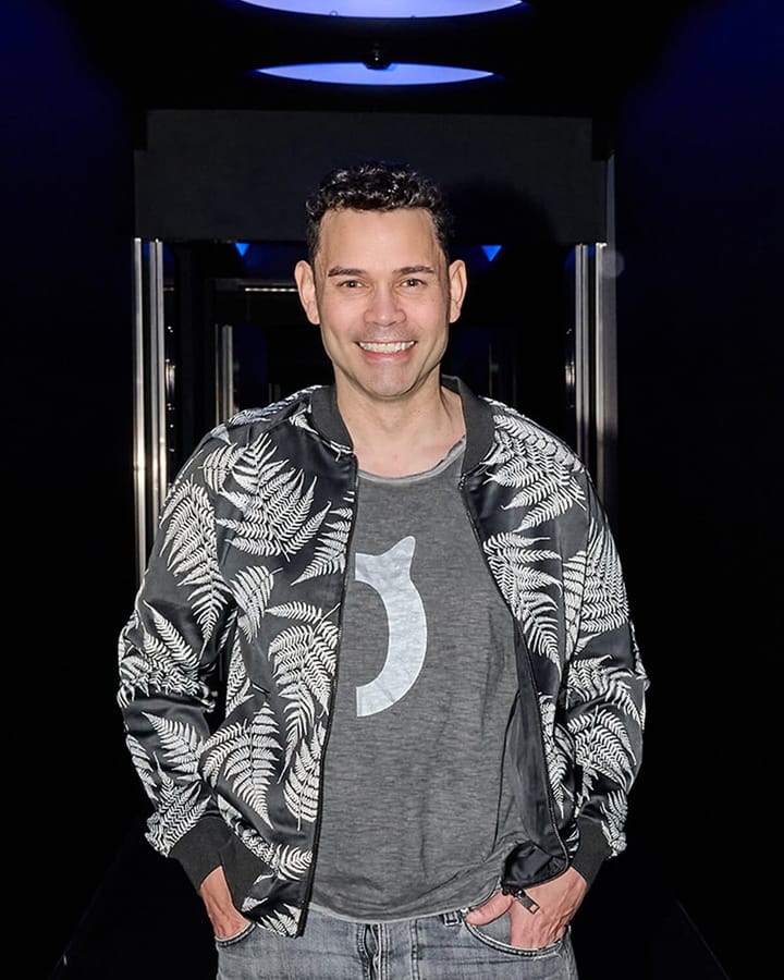 Nigel Camp, London filmmaker, smiling in a fern-print bomber jacket
